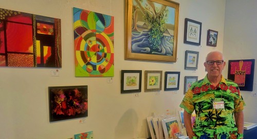 Frank Oliva standing in front of his art displayed at the Windward Artists Guild Holiday Fair - The Arts at Marks Garage - Dec 8 - 14, 2022