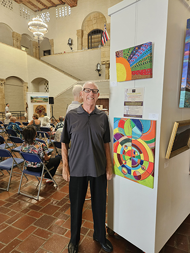 Frank Oliva standing in front of his art exhibit at Pamana Art Exhibit
