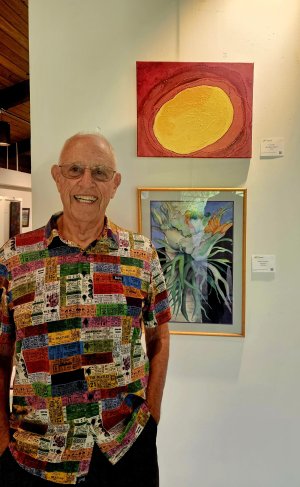 Artist standing in front of two paintings while wearing a very colorful shirt