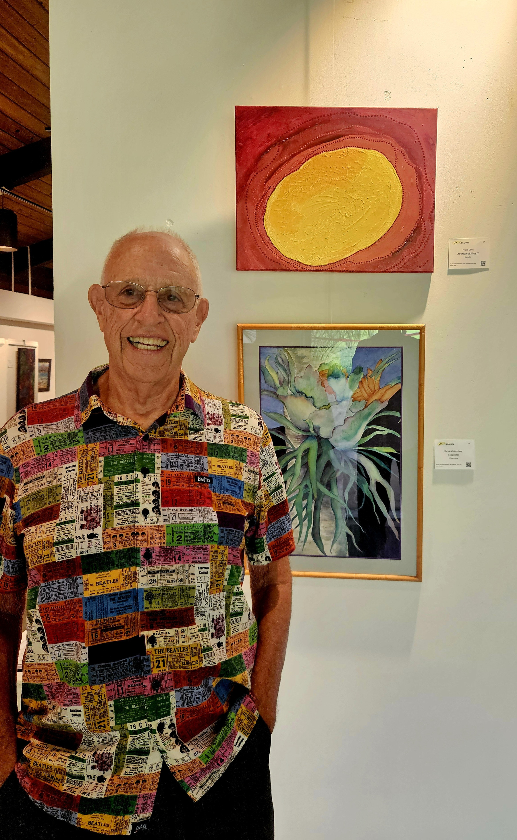 Artist standing in front of two paintings while wearing a very colorful shirt